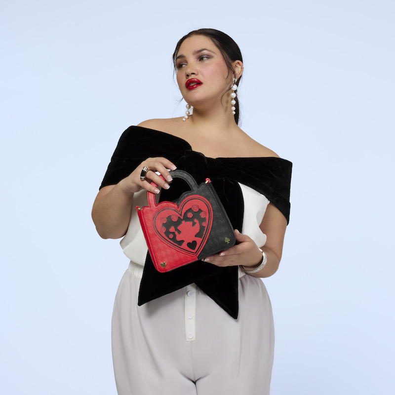 Woman wearing a black and white body suit, holding the Loungefly Queen of Hearts crossbody bag. She stands against a light blue background. 
