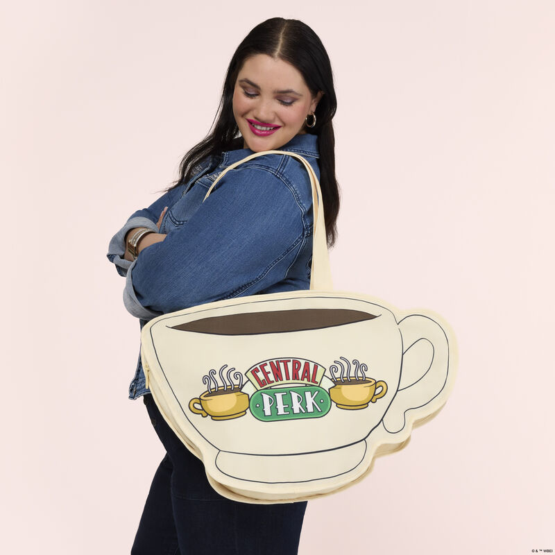 Woman wearing black pants and a denim top. She wears the Loungefly Friend Central Perk Coffee Cup Tote Bag over a shoulder. 